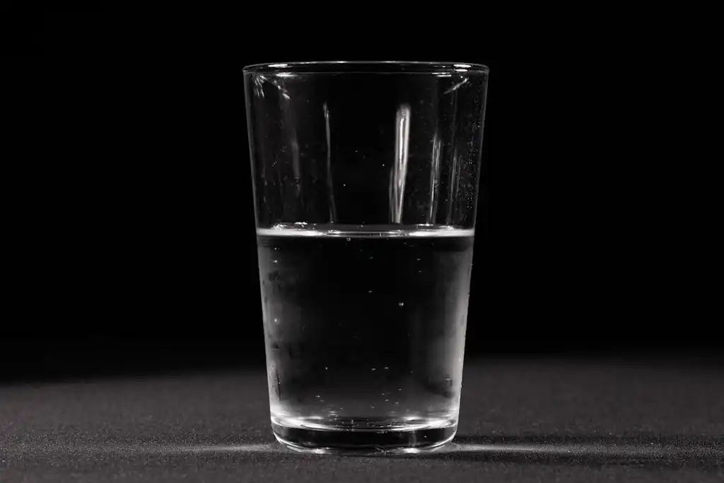 A plain drinking glass filled with water, lit against a dark background.
